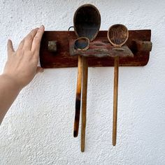 a hand is holding two spoons on a rack with wooden utensils hanging from it