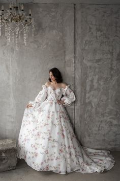 a woman in a white dress leaning against a wall with a chandelier hanging from the ceiling