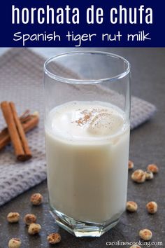 a glass filled with milk sitting on top of a table next to cinnamon sticks and nuts