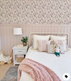 a white bed sitting next to a pink wall with flowers on it and a lamp