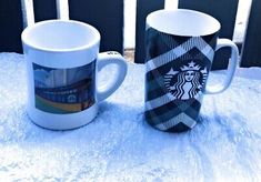 two starbucks mugs sitting on top of a table covered in snow