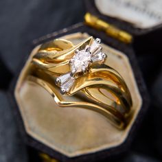 two gold wedding rings sitting on top of each other in front of a hexagonal box