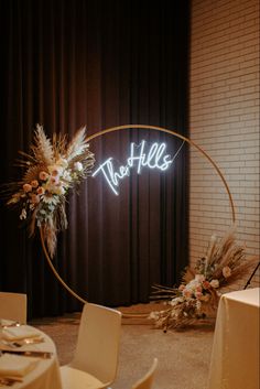 the tables are set up with white linens and flowers in front of a circular neon sign