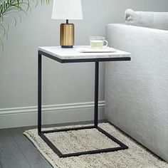 a small table with a lamp on it next to a couch and potted plant