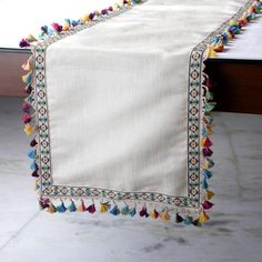 a table runner with colorful tassels on it and a white cloth draped over the edge