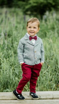 a young boy in a suit and bow tie standing on a wooden platform near tall grass