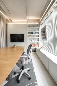 an empty conference room with a large wooden table and white office chairs in front of a flat screen tv mounted on the wall