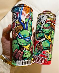 a person holding up two cans of teenage mutant ninjas on the same canister