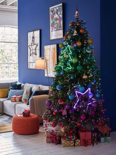 a brightly lit christmas tree stands in the corner of a living room with blue walls