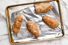 baked potatoes sitting on top of aluminum foil in a baking pan, ready to go into the oven