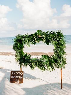 a photo booth sign on the beach with a wreath around it and a camera in front