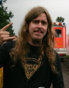 a man with long hair standing in front of a firetruck pointing at the camera