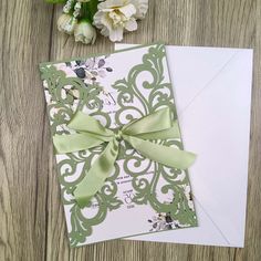 a green and white wedding card with a bow on the front, sitting next to some flowers