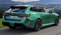 the rear end of a green bmw car on a road with mountains in the background