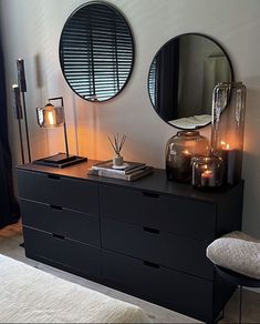 two round mirrors on the wall above a dresser with candles and books in front of it