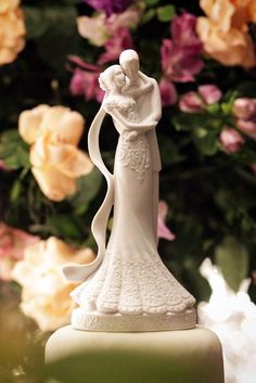 a wedding cake topper with flowers in the background