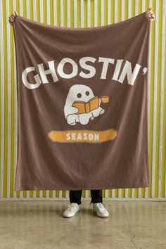 a person standing in front of a wall holding up a brown ghostin'season banner