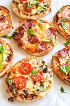 several small pizzas with toppings on top of white paper and green leafy garnish