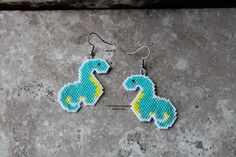 a pair of beaded dinosaur earrings sitting on top of a stone floor next to each other