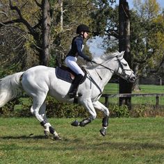 a woman riding on the back of a white horse through a lush green field next to trees