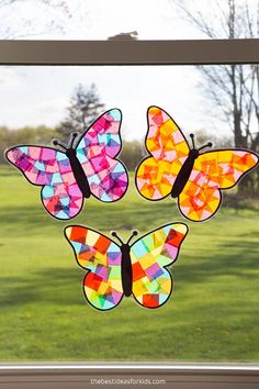 four stained glass butterflies sitting on top of a window sill in front of a grassy field