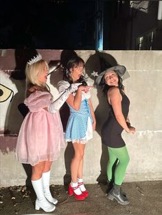 three women dressed in costumes standing next to each other near a wall with graffiti on it