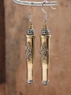 pair of earrings with gold and silver details hanging from a hook on a metal bar