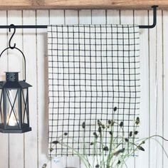 a black lantern hanging from a wooden shelf next to a vase with flowers and a tea towel