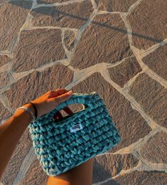 a hand holding a blue purse on top of a stone floor