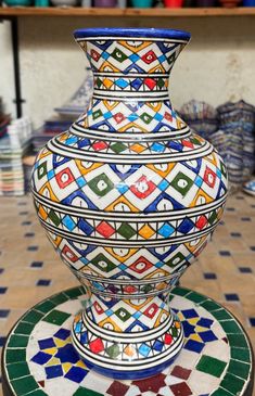 a colorful vase sitting on top of a tile floor next to a shelf filled with pottery