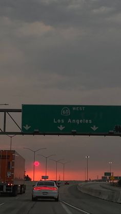 an exit sign for the west and los angeles freeway at dusk with traffic going underneath it