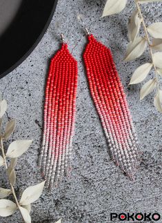 two pairs of red and silver beaded earrings on top of a table next to leaves