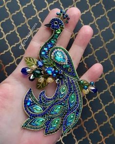 a peacock brooch sitting on top of a person's hand