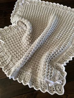 a white crocheted blanket on top of a wooden floor next to a pair of scissors