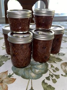 four jars filled with jam sitting on top of a tablecloth covered table next to a window