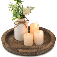 three lit candles on a wooden tray with flowers and greenery in a vase next to them