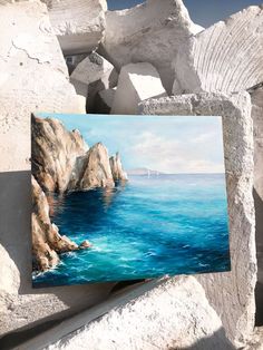 a painting is displayed on some rocks by the ocean