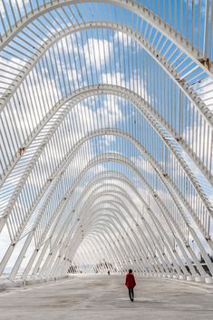 a person in a red jacket is walking under a large white structure with metal beams