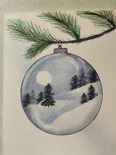 a christmas ornament hanging on a tree branch with snow and pine trees in the background