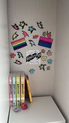 some books are sitting on top of a white shelf in front of a wall with colorful stickers