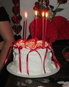 a white cake with red ribbon and lit candles