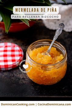 a jar filled with orange marmalade on top of a table next to a potted plant