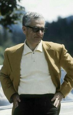 an older man standing in front of a car with his hands on his hips wearing sunglasses