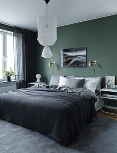 a bedroom with dark green walls and grey bedding, two lamps on either side of the bed