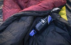 an open sleeping bag sitting on top of a pile of blankets and pillows with a water bottle next to it