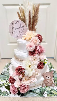 a three tiered cake with flowers and feathers on the top is decorated with a teddy bear