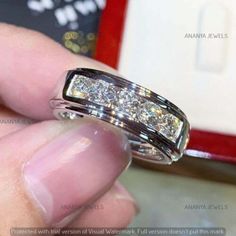 someone is holding a wedding ring with three diamonds on it's sides and the other side has a red box in the background