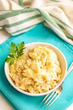 a bowl of cheesy brown rice on a blue place mat with a fork