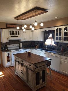 a kitchen with wooden floors and white cabinets, an island in the middle is surrounded by hanging lights