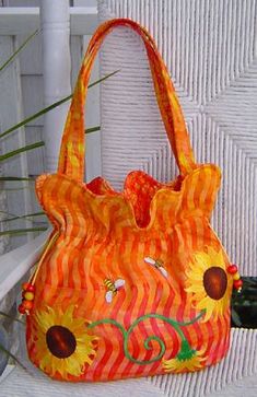 an orange handbag with sunflowers on it sitting on a chair next to a plant